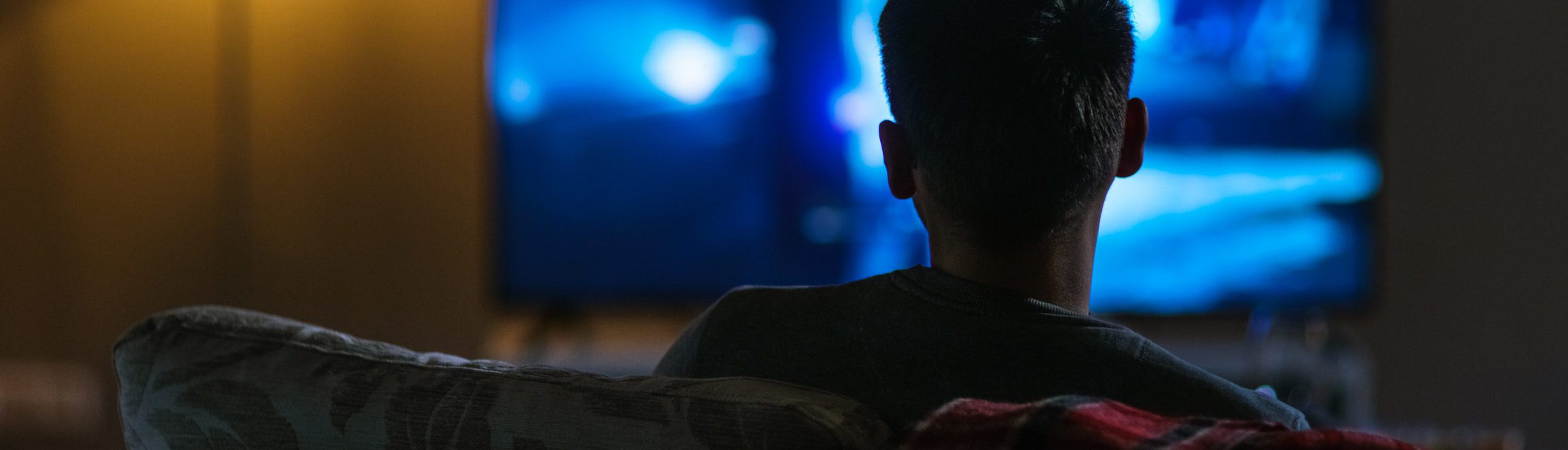 Back View of a Man Sitting on a Couch Watching Movie on His Big Flat Screen TV.